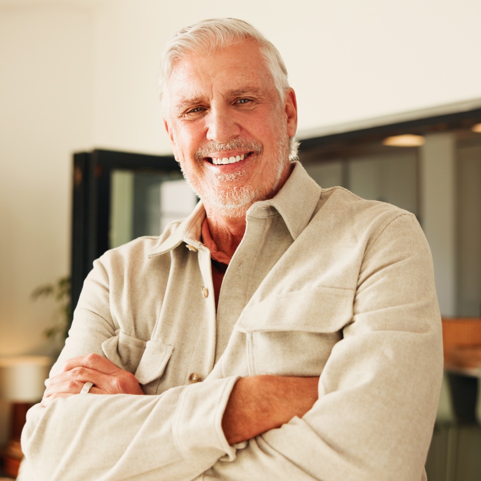 Arms crossed, smile and portrait of old man in home for retirement, peace and confidence. Happiness, calm and weekend break with senior person in living room of apartment for positive attitude.