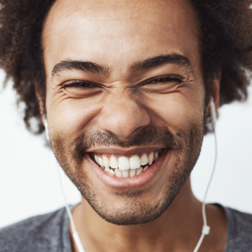 Close up portrait of young happy african man smiling listening to upbeat streaming music laughing over white background. Youth concept. Copy space.