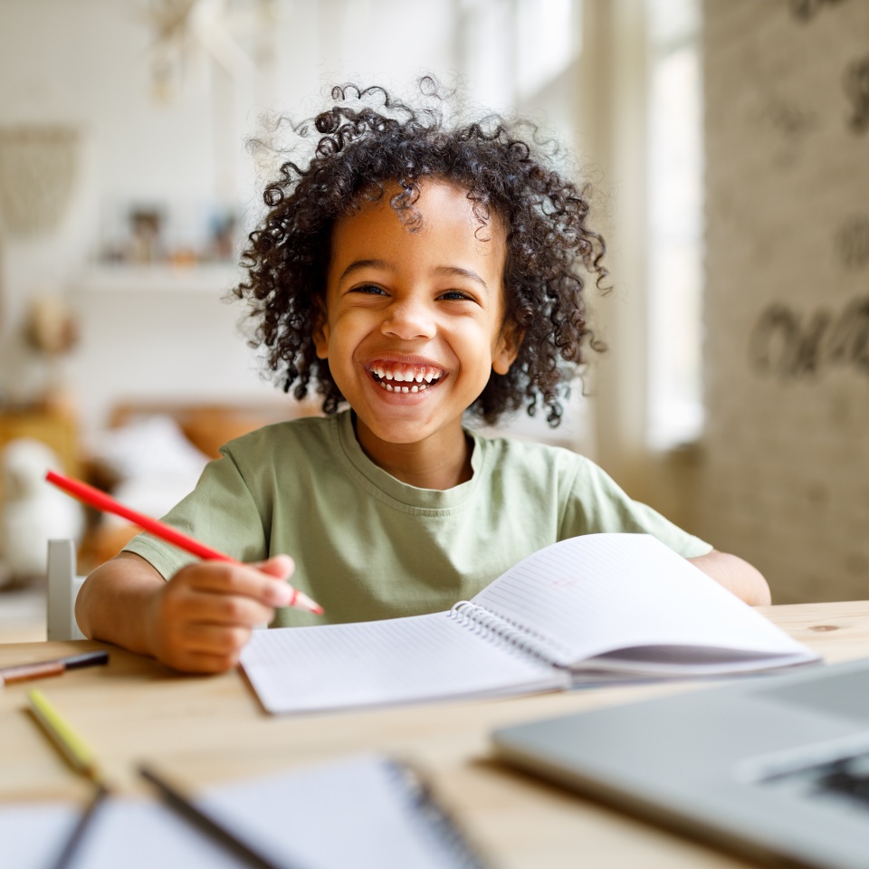Distance education. Smiling african american child schoolboy studying online on laptop at home, sitting at table and communicating with teacher through video call on computer