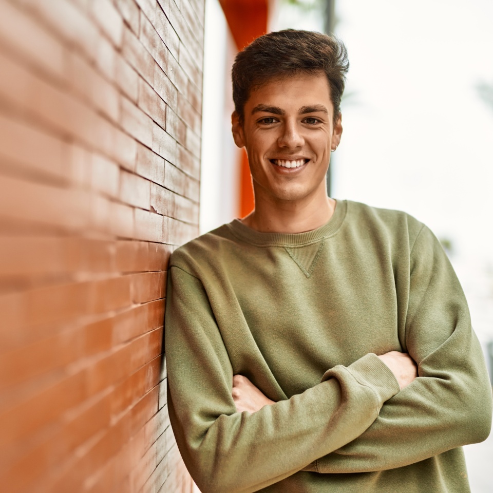 Young hispanic man smiling happy with arms crossed gesture at the city.