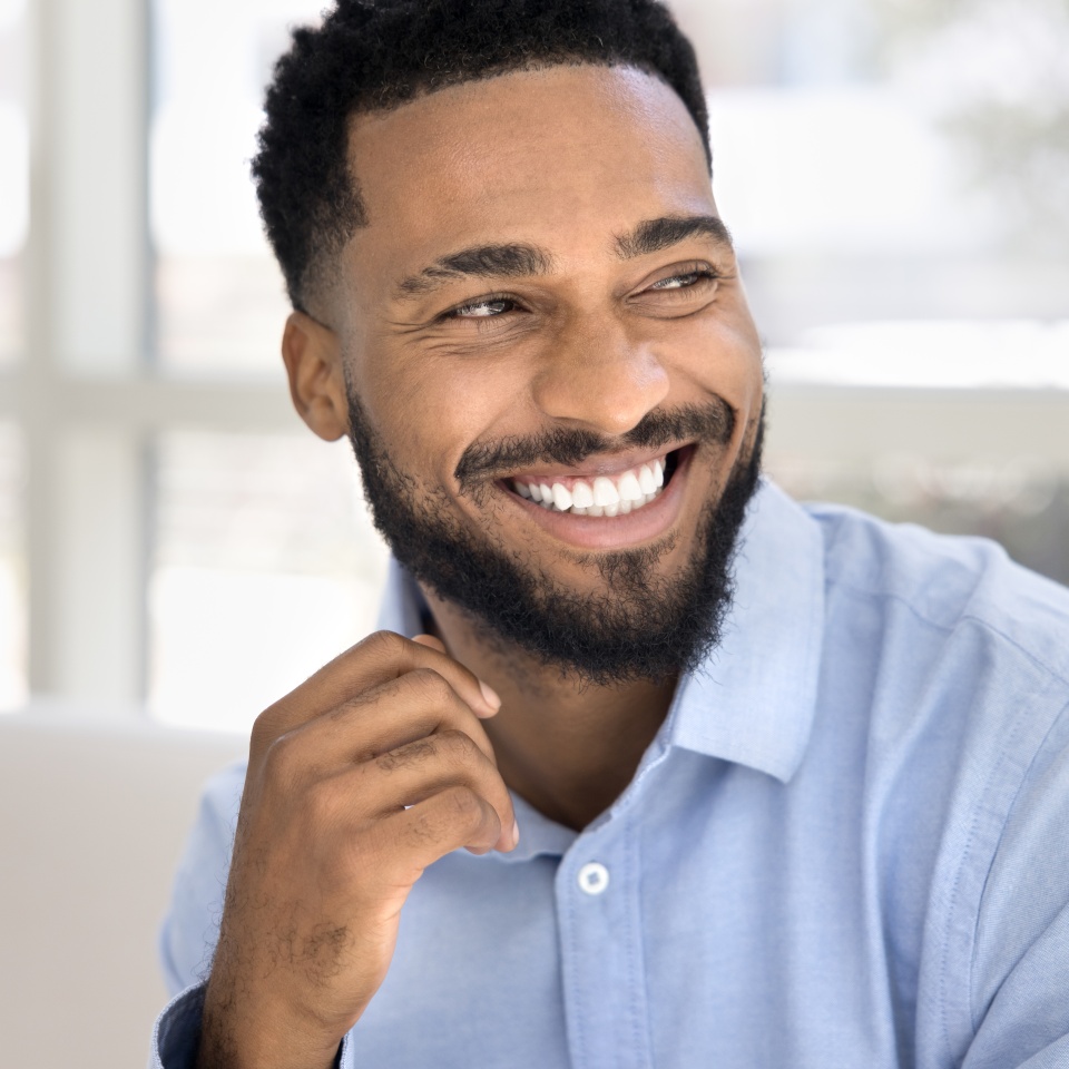 Cheerful attractive young Black man casual indoor portrait. Happy confident African professional, businessman, entrepreneur in office shirt looking away with perfect toothy smile
