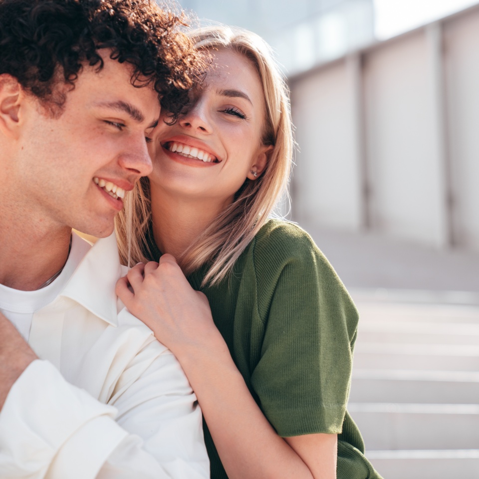 Smiling beautiful woman and her handsome boyfriend. Couple in casual summer clothes. Happy cheerful family. Female and man having fun. They posing in the street in sunny day. Sit at stairs