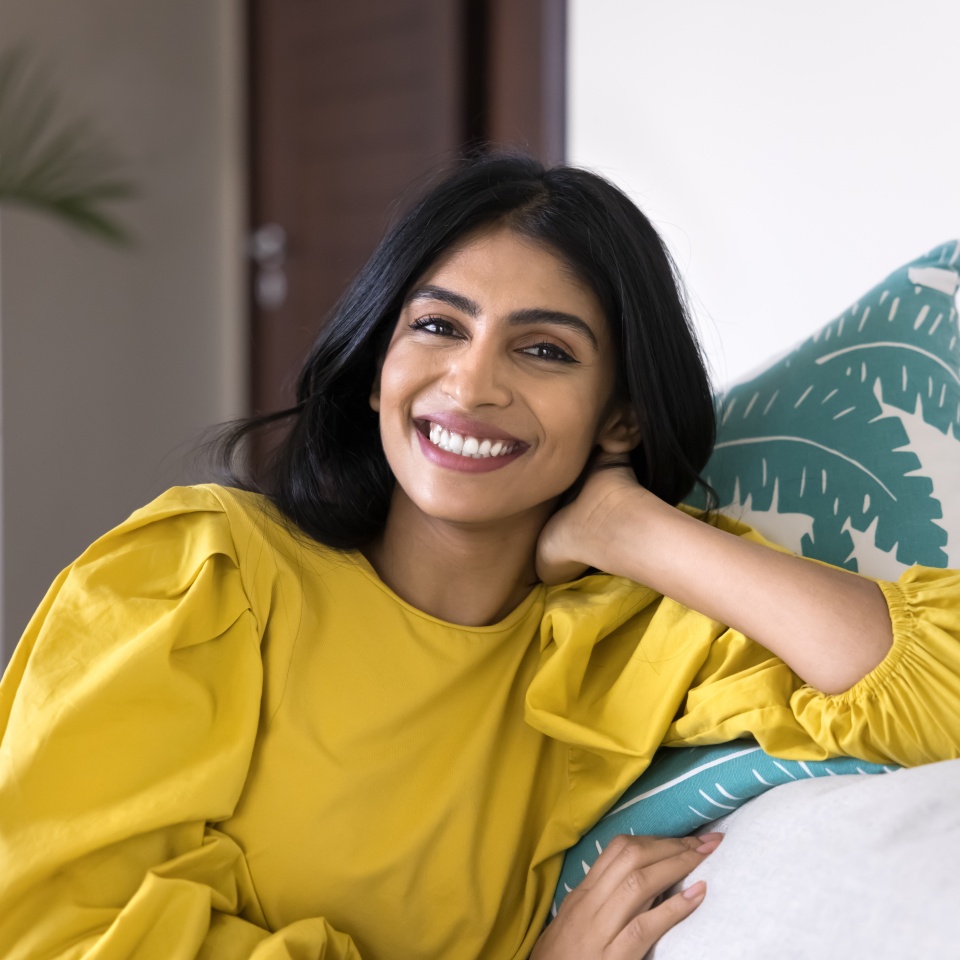 Portrait of happy Indian woman relaxing on comfortable couch, leaned on cushion, laughing, stare at camera, exuding satisfaction, enjoy pleasant, carefree daytime rest, weekend alone at modern home